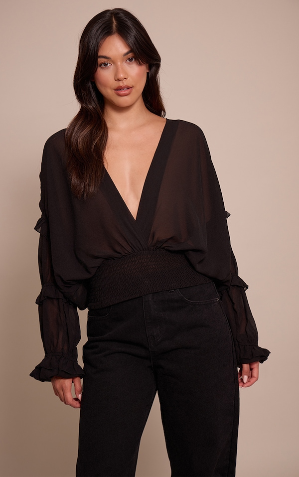 Blouse noire en mousseline de soie, à décolleté plongeant et détails à volants.